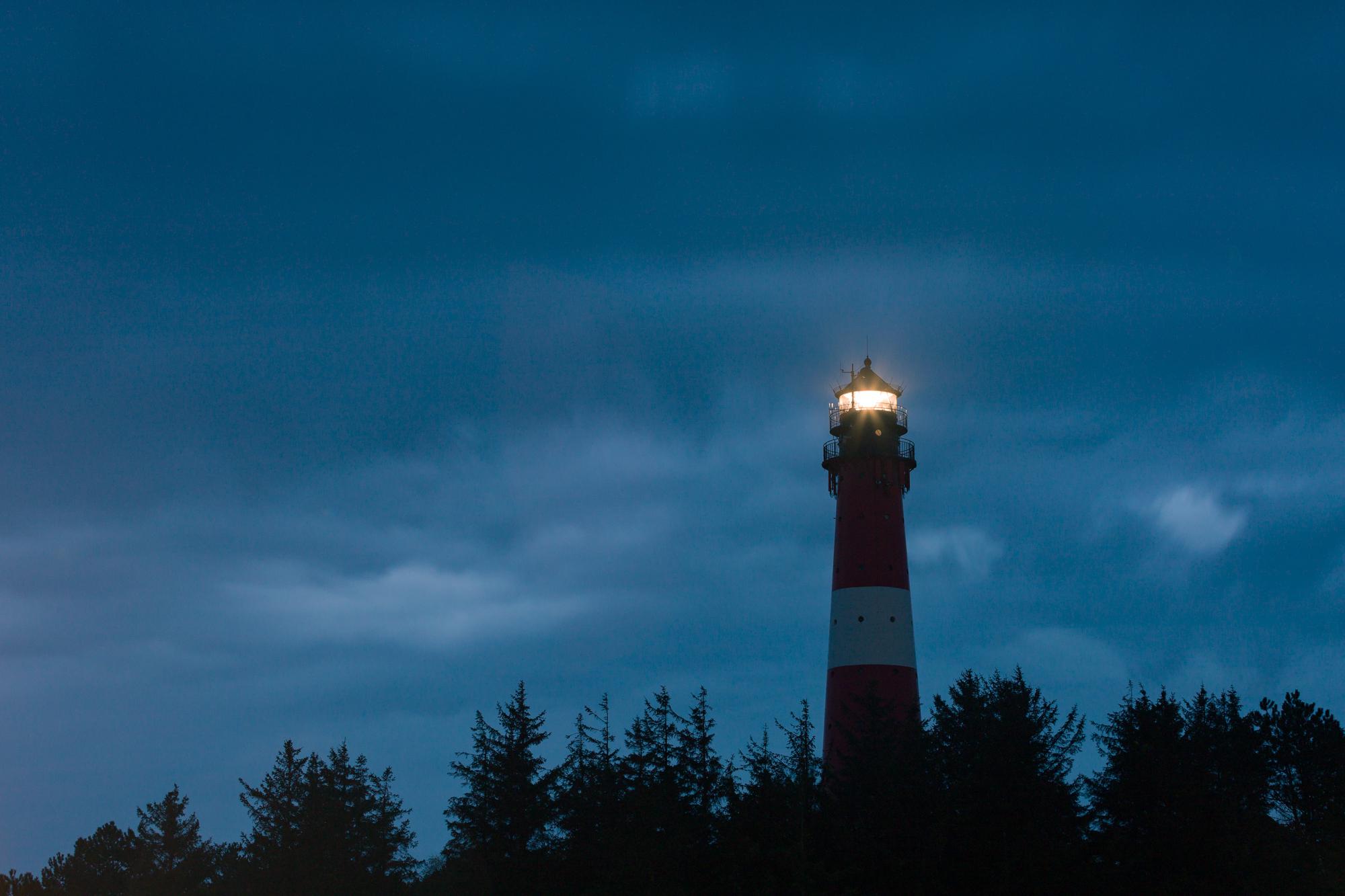 Light rain softens the sky. A long exposure catches the bright signal of this lighthouse.