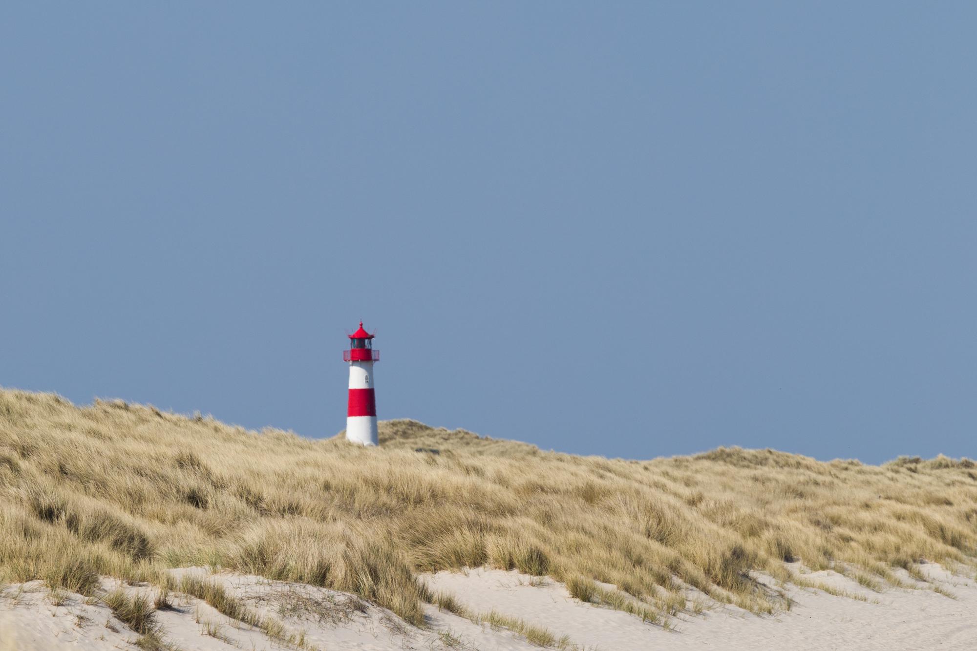 The lighthouse stands out from the beach grass with its bright red and white colors. On a clear day, the blue sky provides contrast for the lighthouse.
